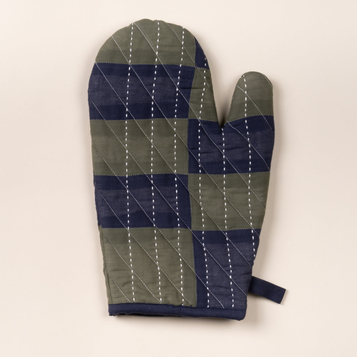 Quilted oven mitt with green and navy patchwork pattern and white stitched lines, shown on a neutral background.