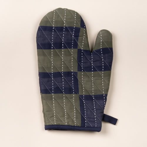 Quilted oven mitt with green and navy patchwork pattern and white stitched lines, shown on a neutral background.