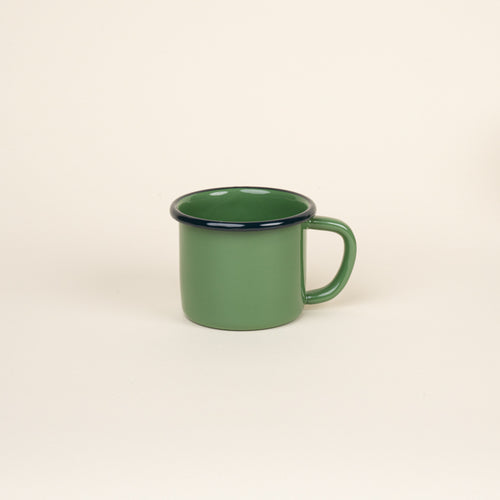 A green enamel mug with a dark rim and handle, shown against a neutral beige background.
