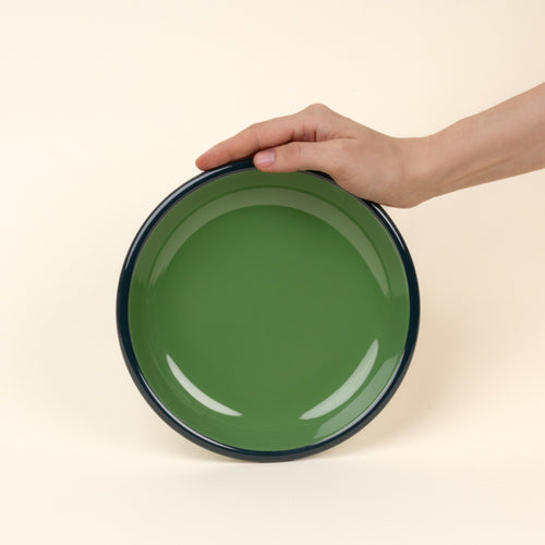 A hand props up an enamel side plate in green with an dark rim.