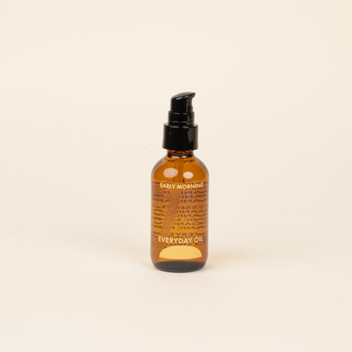 Amber glass bottle with black cap and label that reads 'Early Morning Everyday Oil' on a beige background.