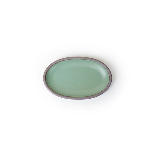 A small oval ceramic platter in a green color featuring iron speckles and an unglazed rim