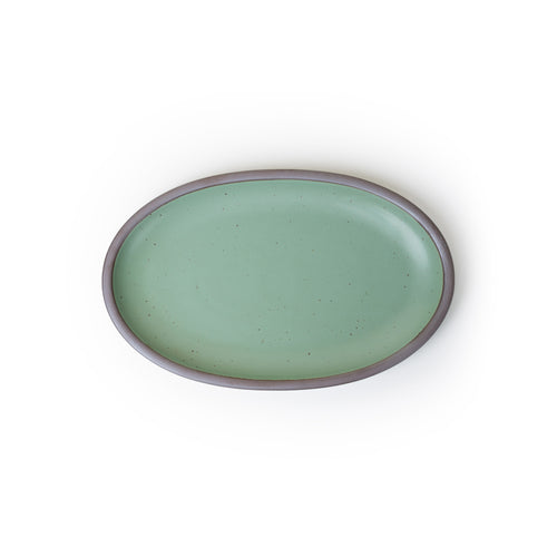 A medium oval ceramic platter in a green color featuring iron speckles and an unglazed rim