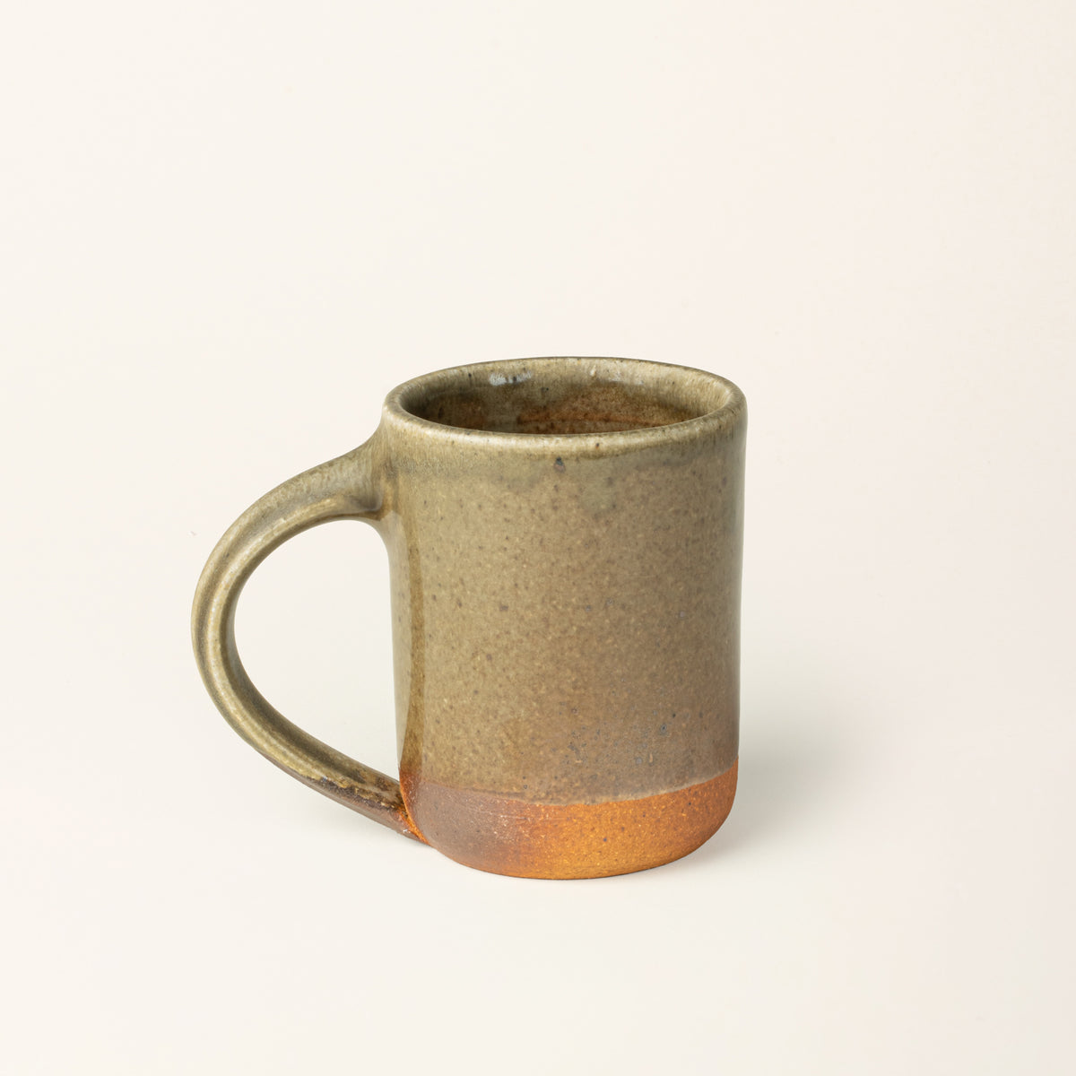 A handmade ceramic mug with a wood fired light earthy green glaze with an unglazed base.