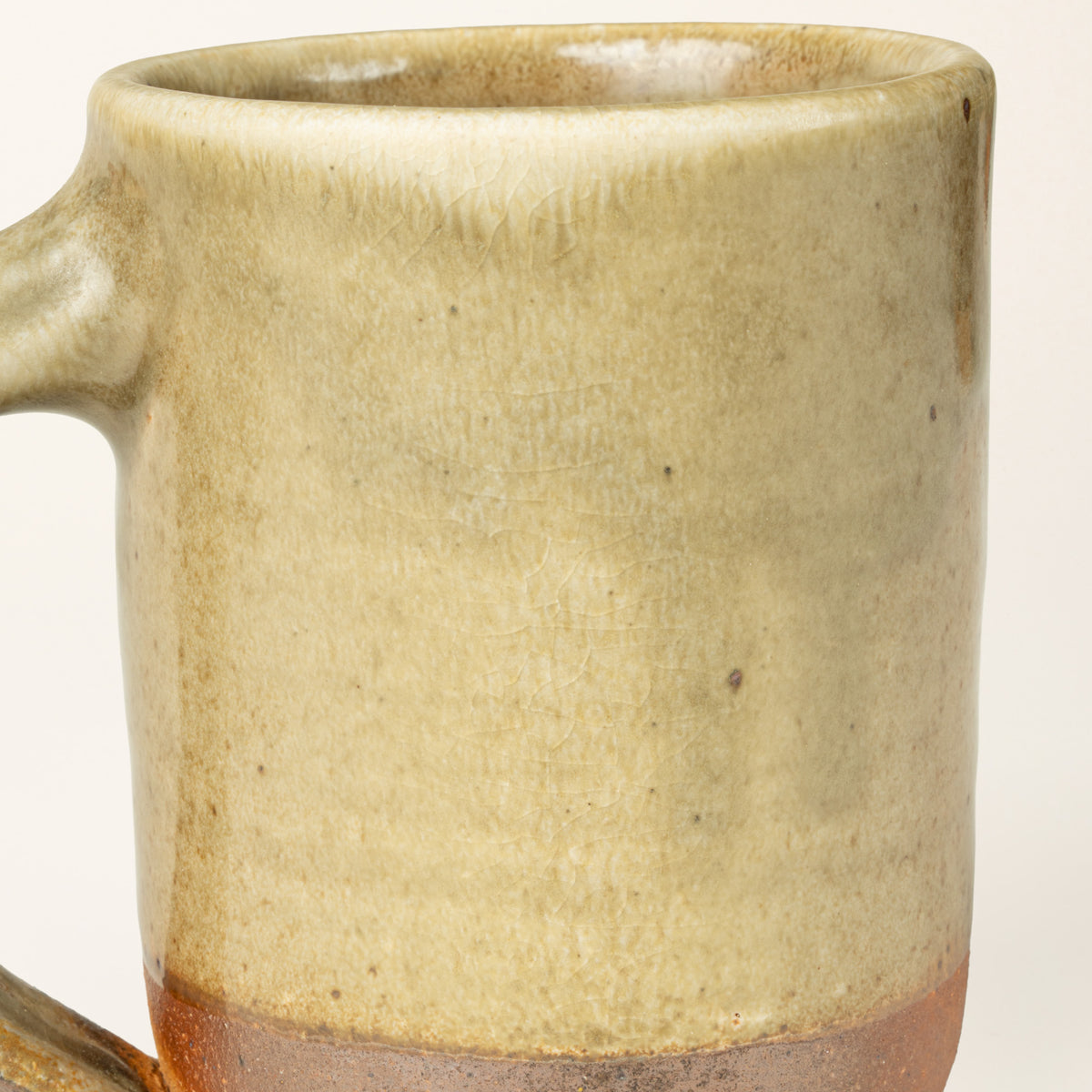 Close-up of a handmade ceramic mug with a textured, rustic glaze showing a gradient from light beige at the top to a warm green at the base, on a white background.