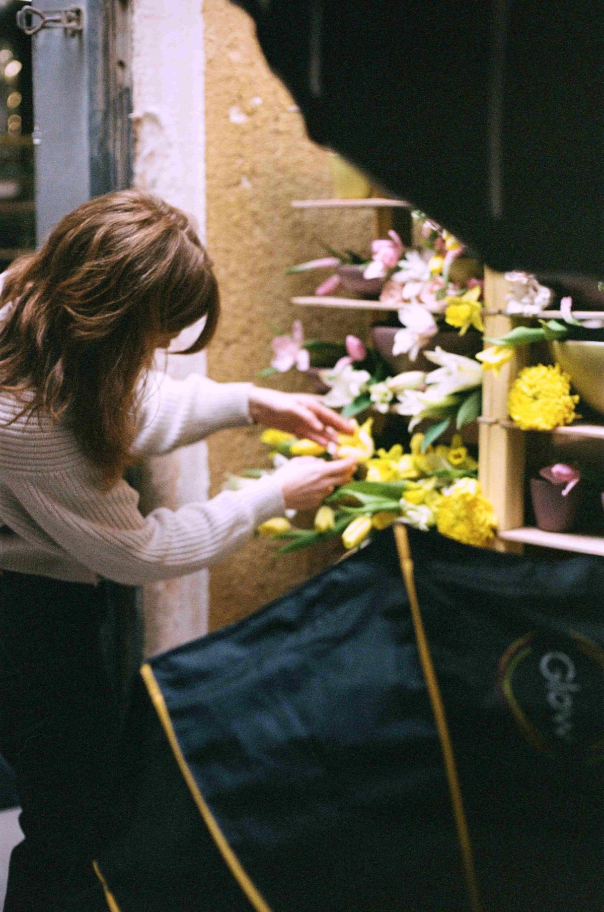 Nicole styling flowers on a kiln cart filled with yellow and soft mauve purple pottery for a photoshoot.