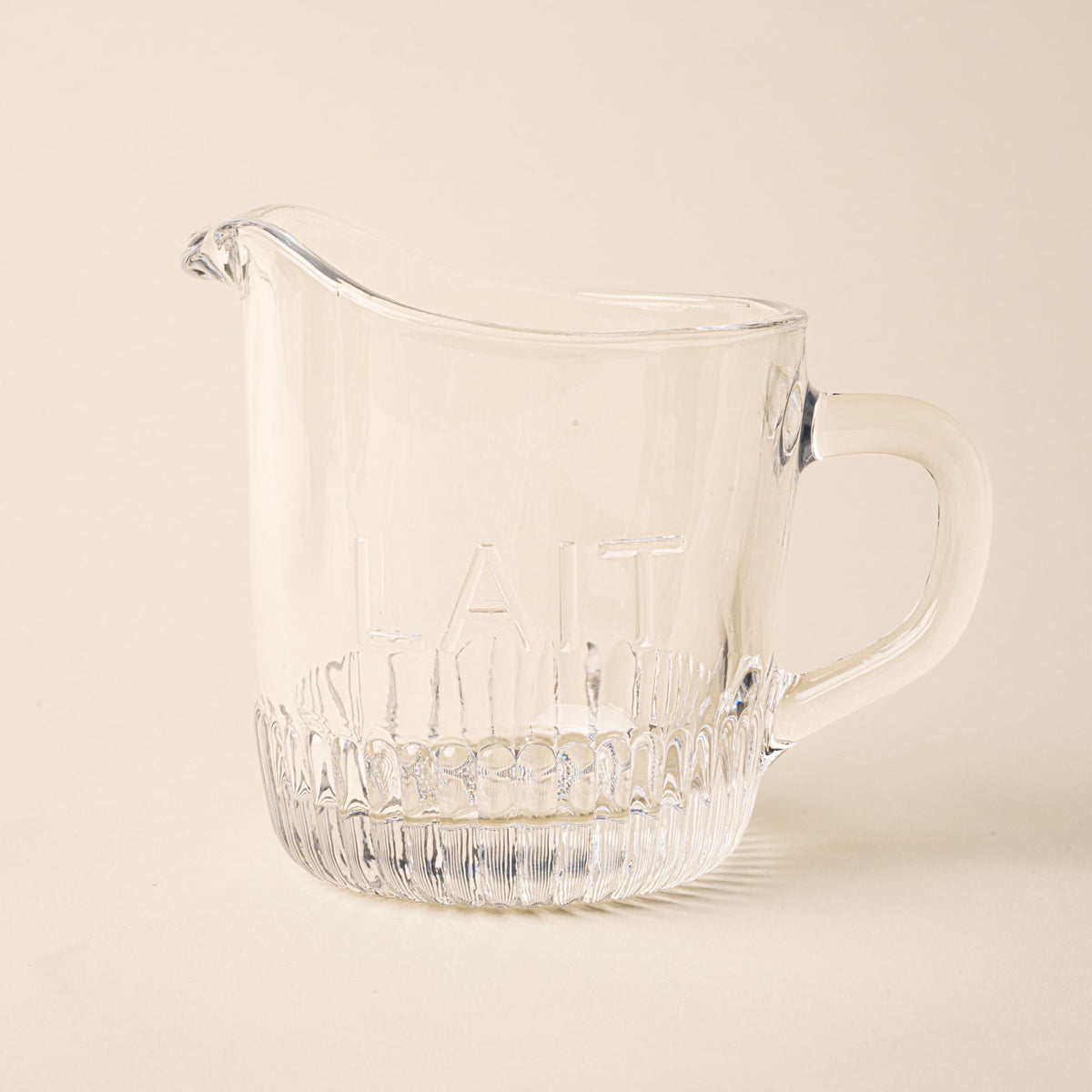 Clear glass pitcher with handle and spout on a light background