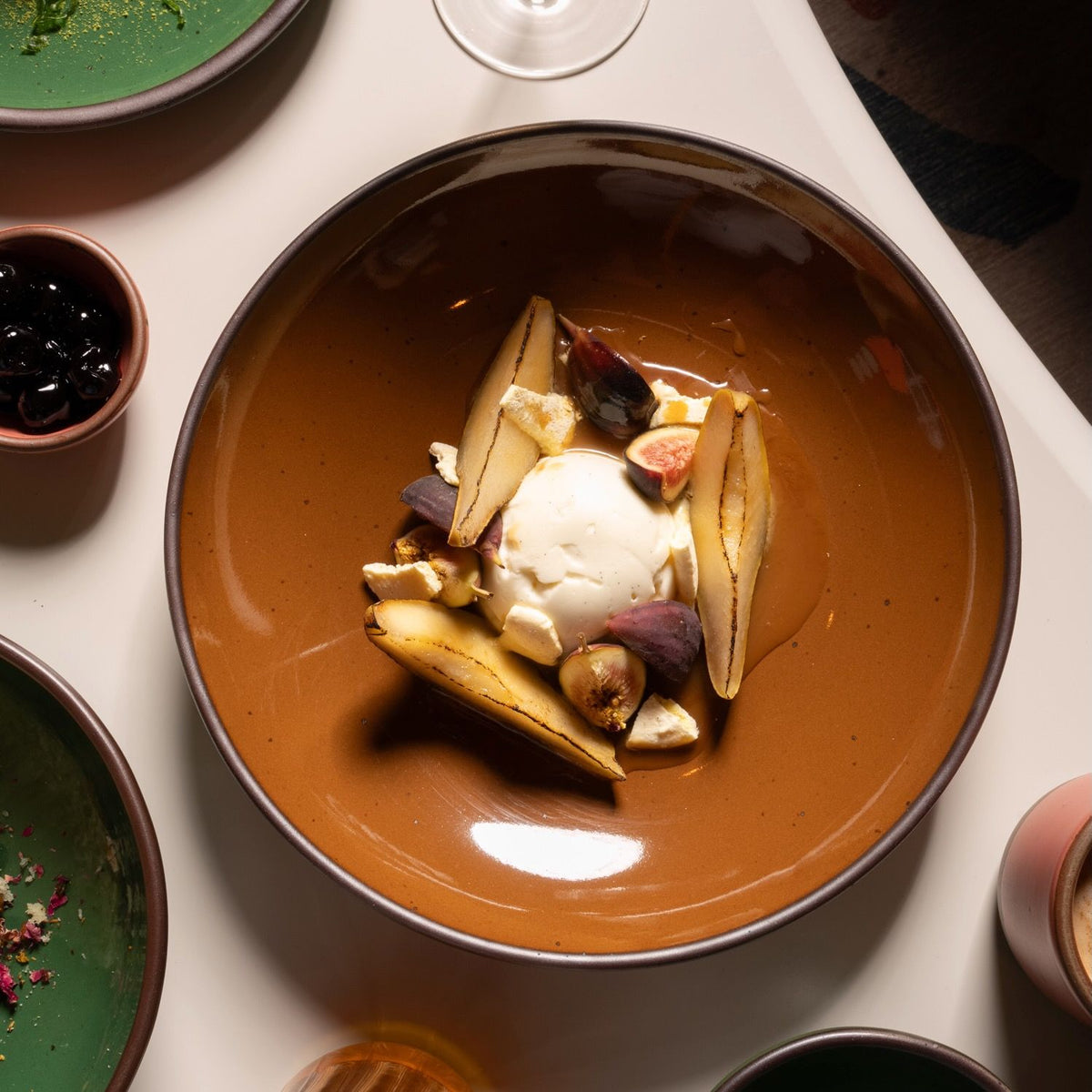Ceramic coupe-plate with vanilla ice cream, roasted fruit, figs, and honey in a warm ceramic setting.