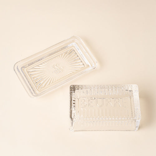 Clear glass butter dish with lid and base on a light background