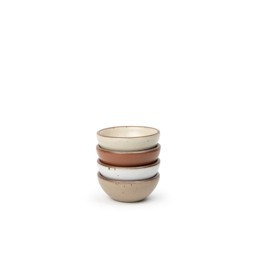 A stack of 4 tiny rounded ceramic bowls in a cool terracotta, warm off-white, cool white, and warm pale brown colors featuring iron speckles and an unglazed rim