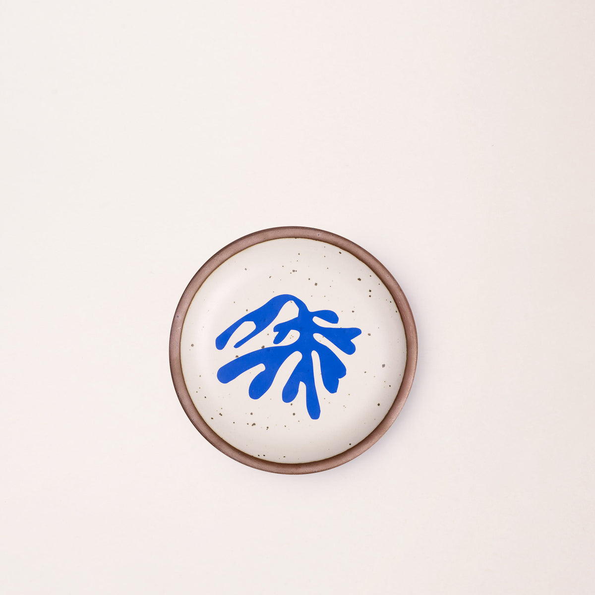 A ceramic dessert sized plates in a warm off-white color with unglazed rim, a frond-like cut-outs from Henri Matisse’s La Perruche et la sirène.