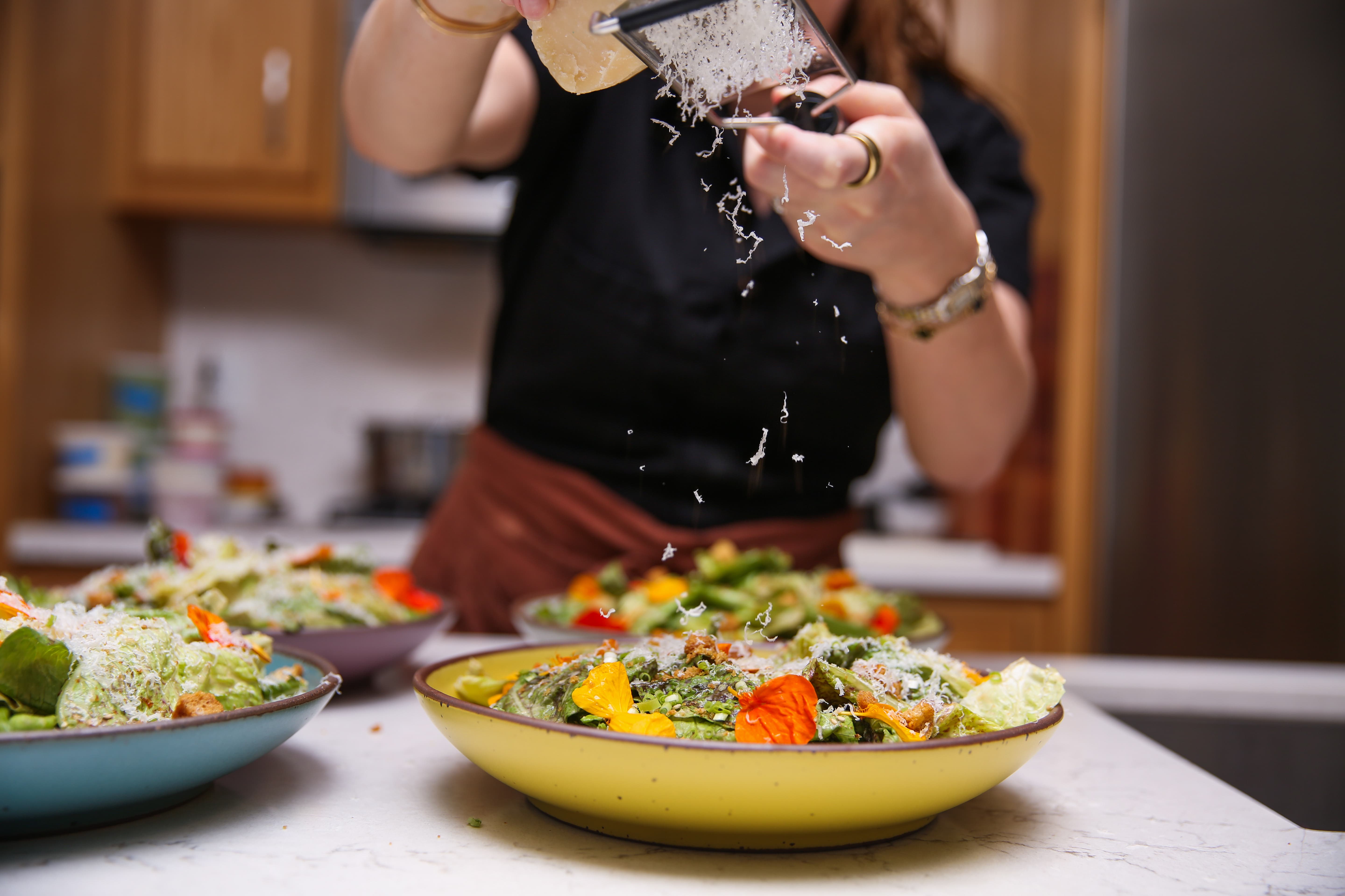 A person grating cheese over beautiful plates of food in a kitchen.