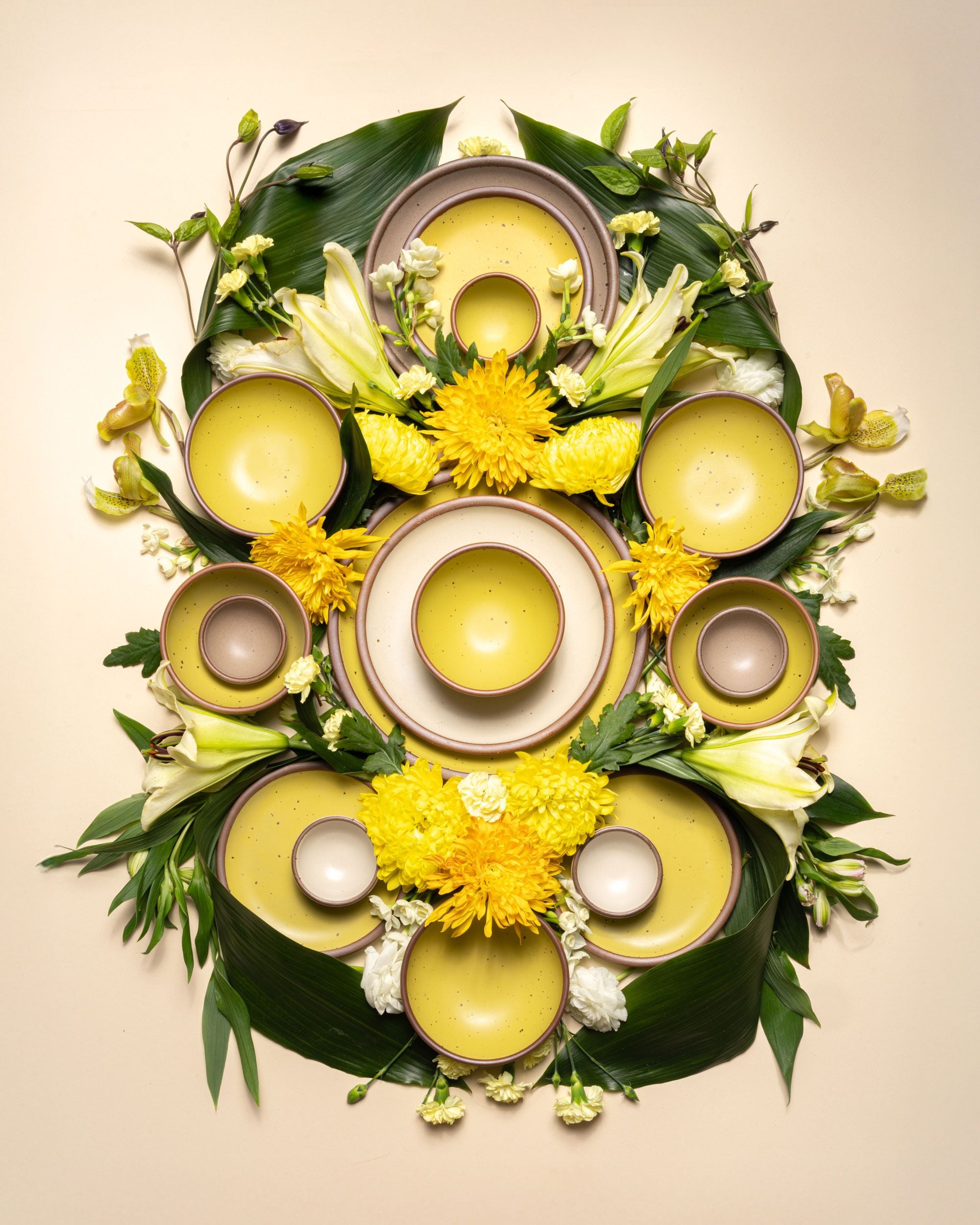 An artful art nouveau inspired styling featuring ceramic bowls in plates in yellow, white, and light pale brown colors with flowers and greenery.