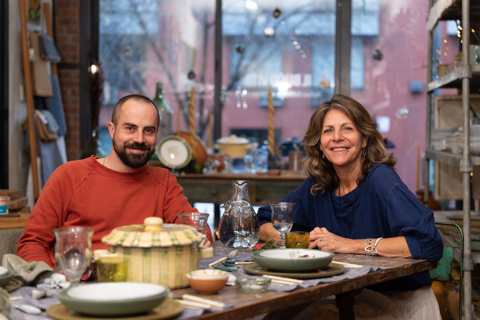 Alex Matisse and Donna Lennard smiling together at a table and staring at the camera.