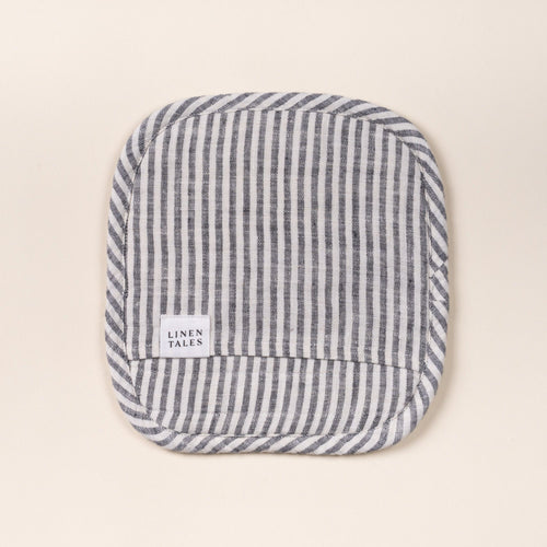 Square quilted linen potholder in a thin striped pattern in white and black colors with rounded corners and a small ‘LINEN TALES’ label, on a light background.