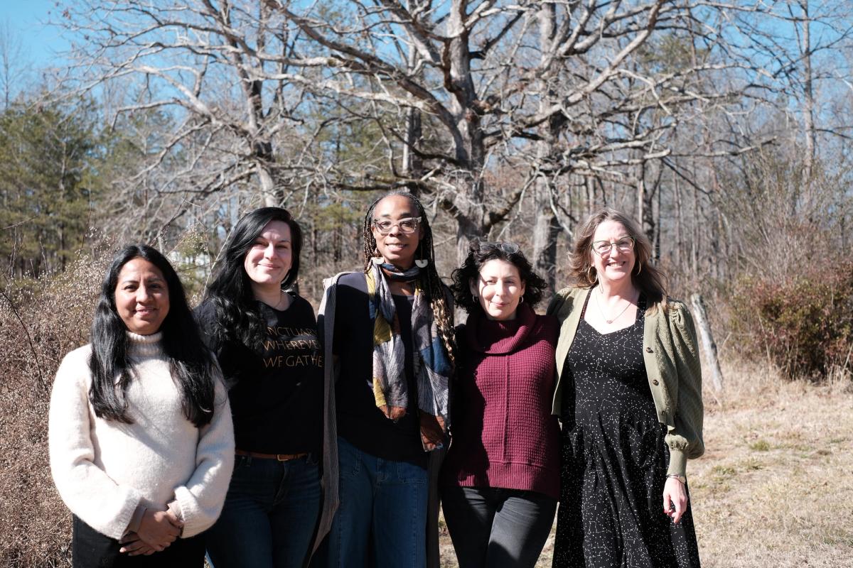 Five women stand together smiling in the outdoors