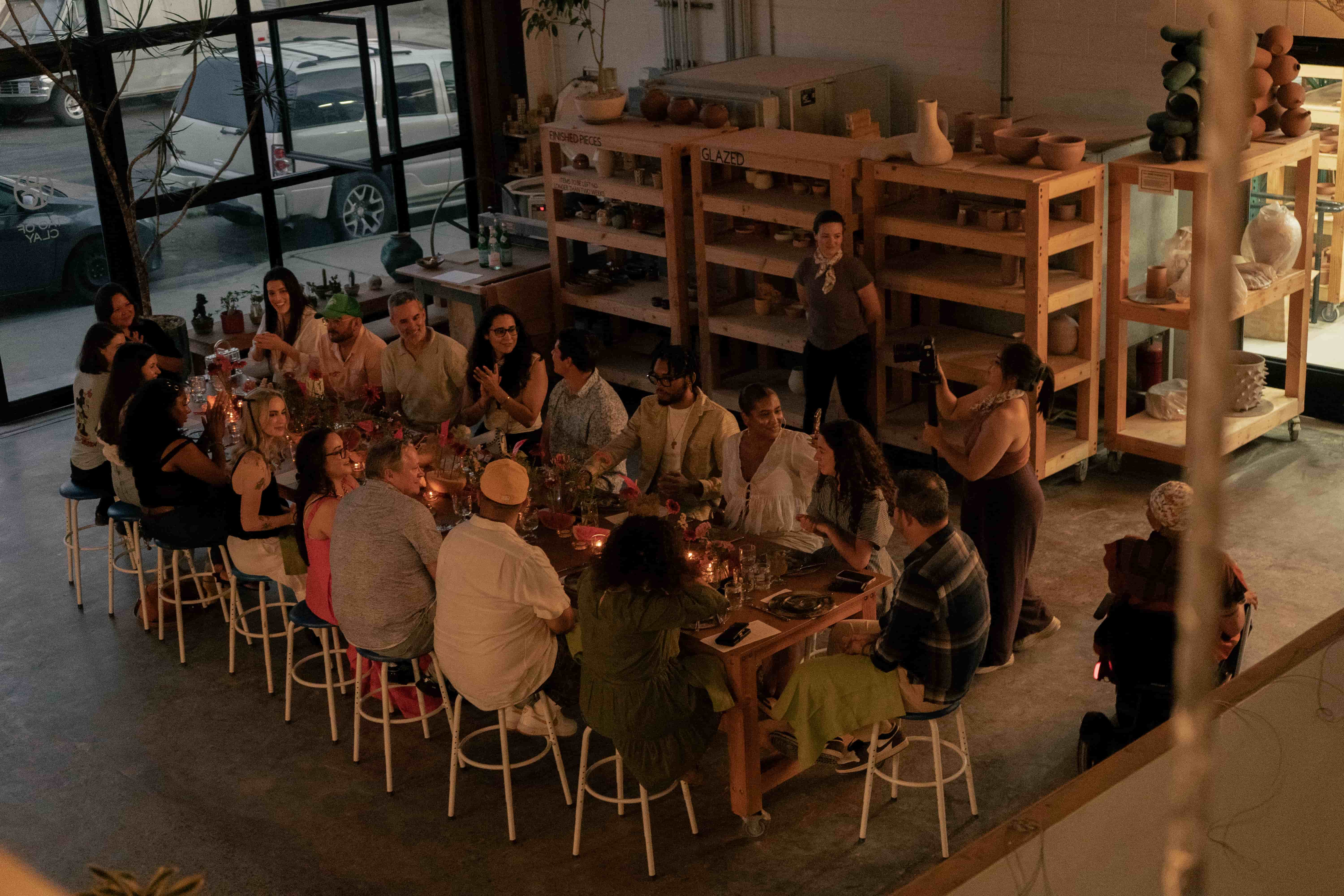 A long table filled with people having dinner and talking, in moody lighting, with fresh flowers as the centerpiece.