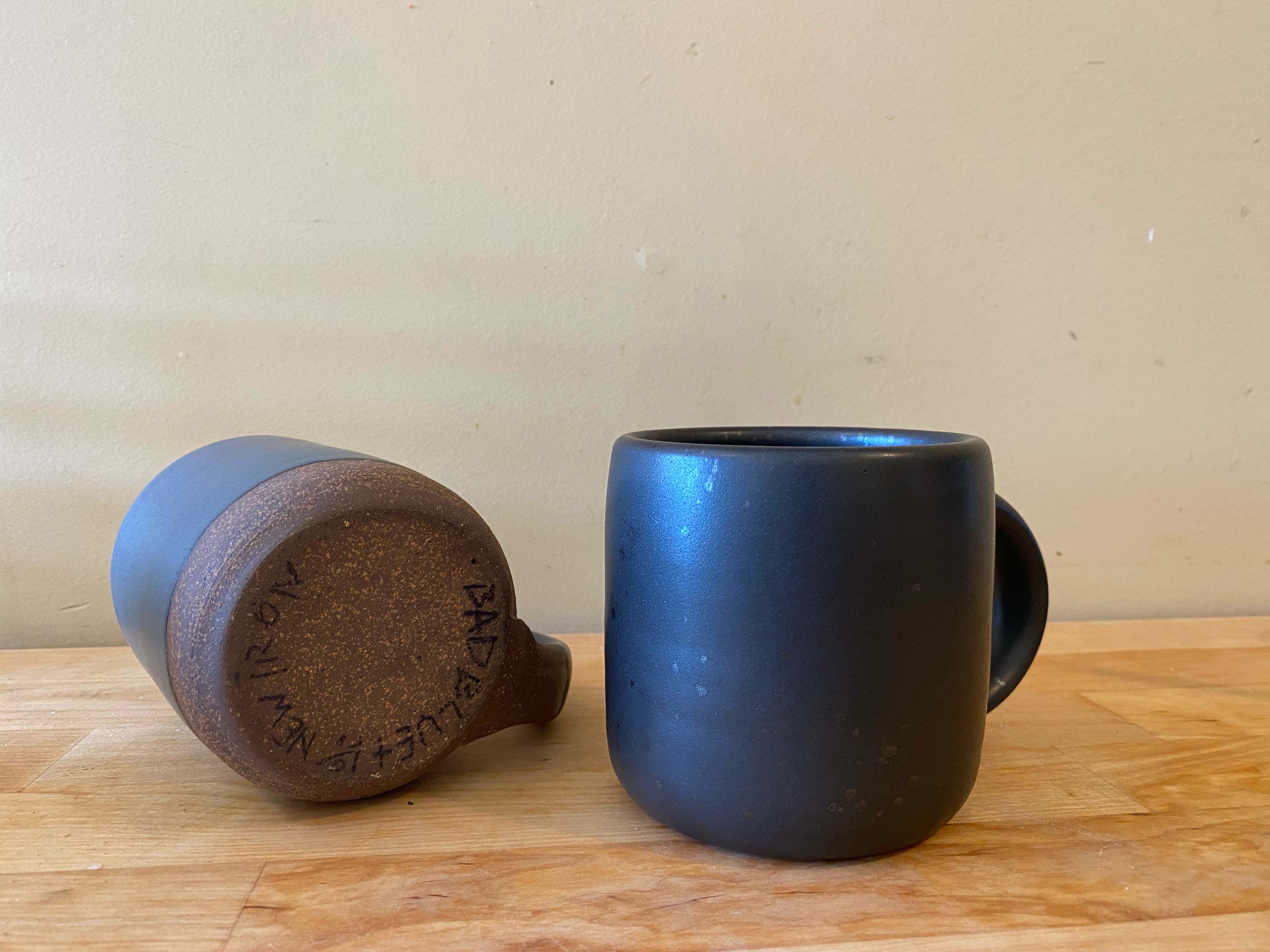 Ceramic mugs in a dark color sit on a wooden slab.