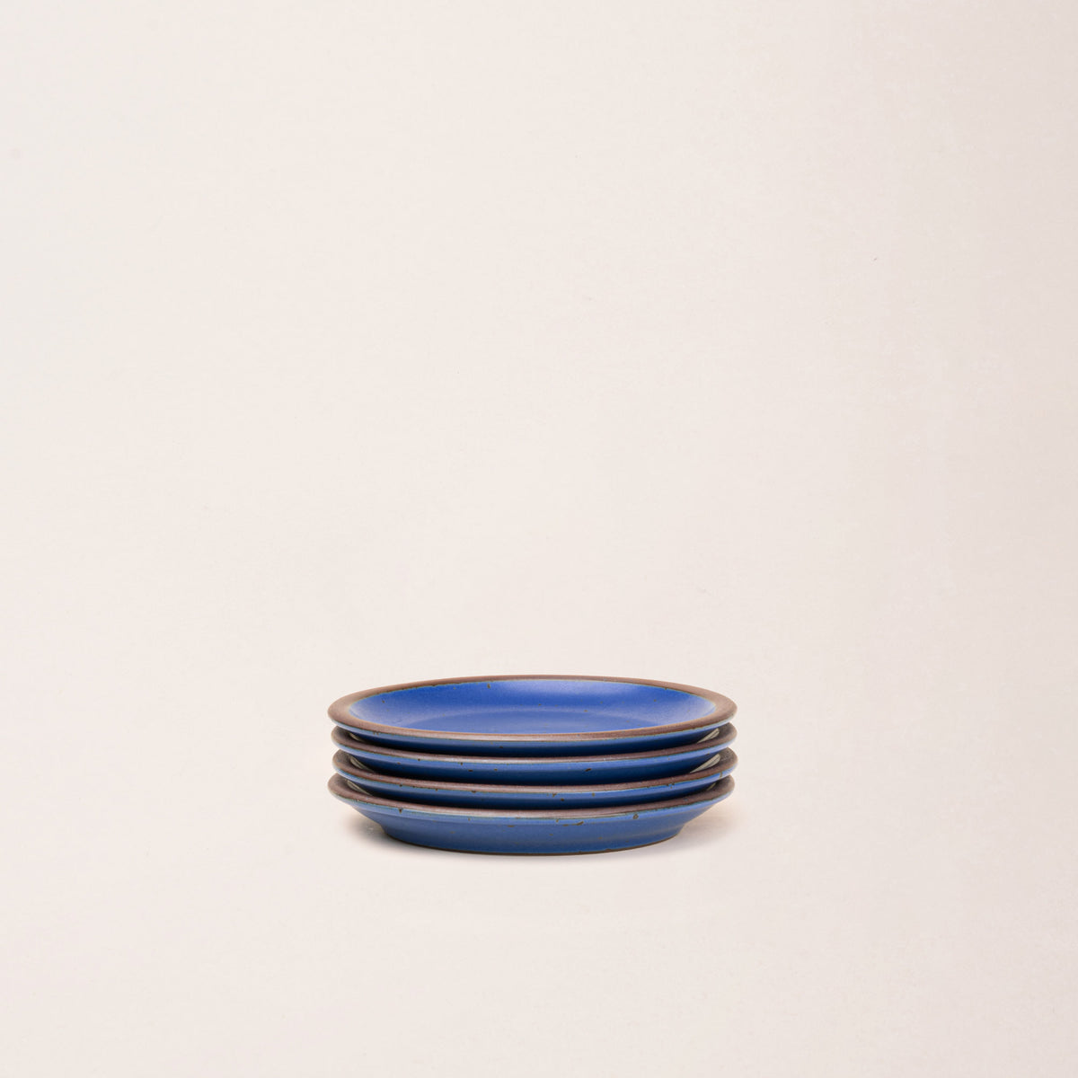 4 dessert sized ceramic plates in a cobalt blue color featuring iron speckles and an unglazed rim.
