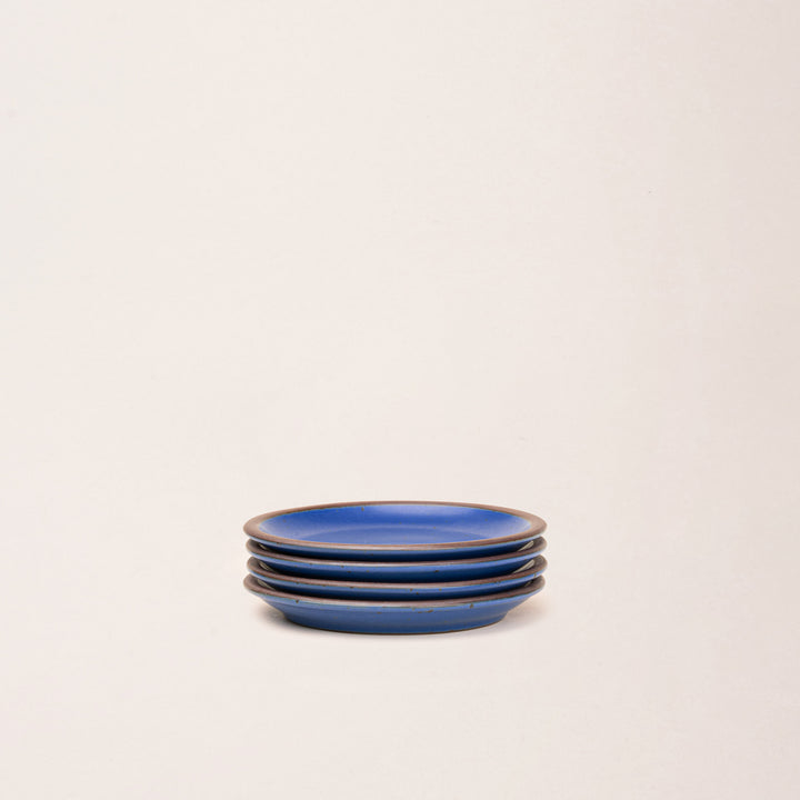 4 dessert sized ceramic plates in a cobalt blue color featuring iron speckles and an unglazed rim.