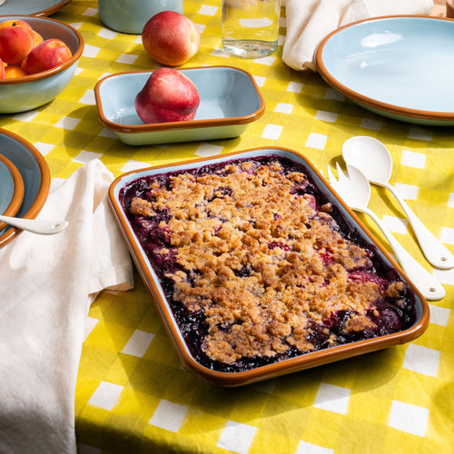 A fruit cobbler in a arge rectangular baking dish in a robin's egg blue color with a warm brown rim; all on a beautiful and colorful table.