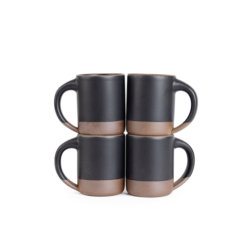 Four medium sized ceramic mugs with handles in a graphite black color featuring iron speckles and unglazed rim and bottom base, stacked in sets of 2.