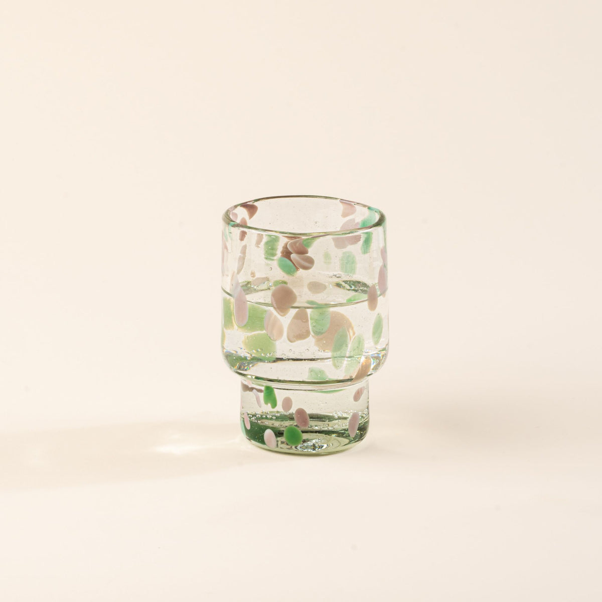 A short clear glass with pastel green and pink speckled patterns, filled with water