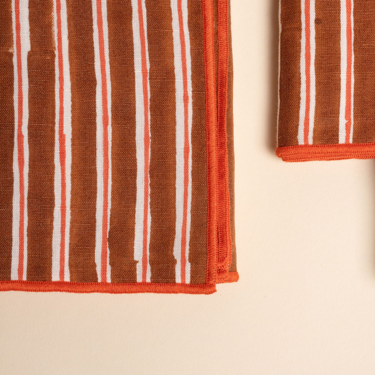 Close-up of a striped cloth napkin showing vertical brown and white stripes with orange accents and a neatly stitched orange edge.
