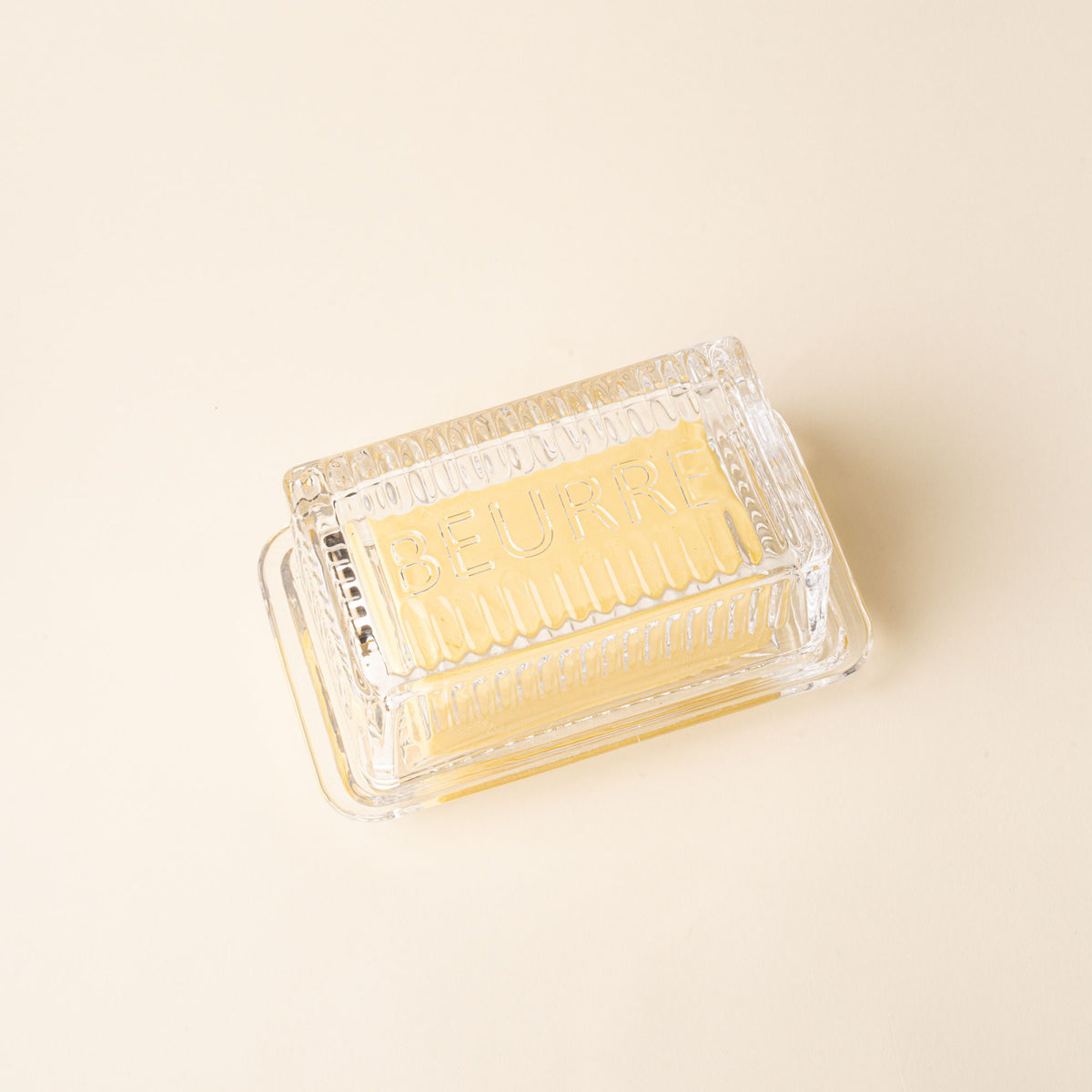 Glass butter dish with lid over butter on a light surface