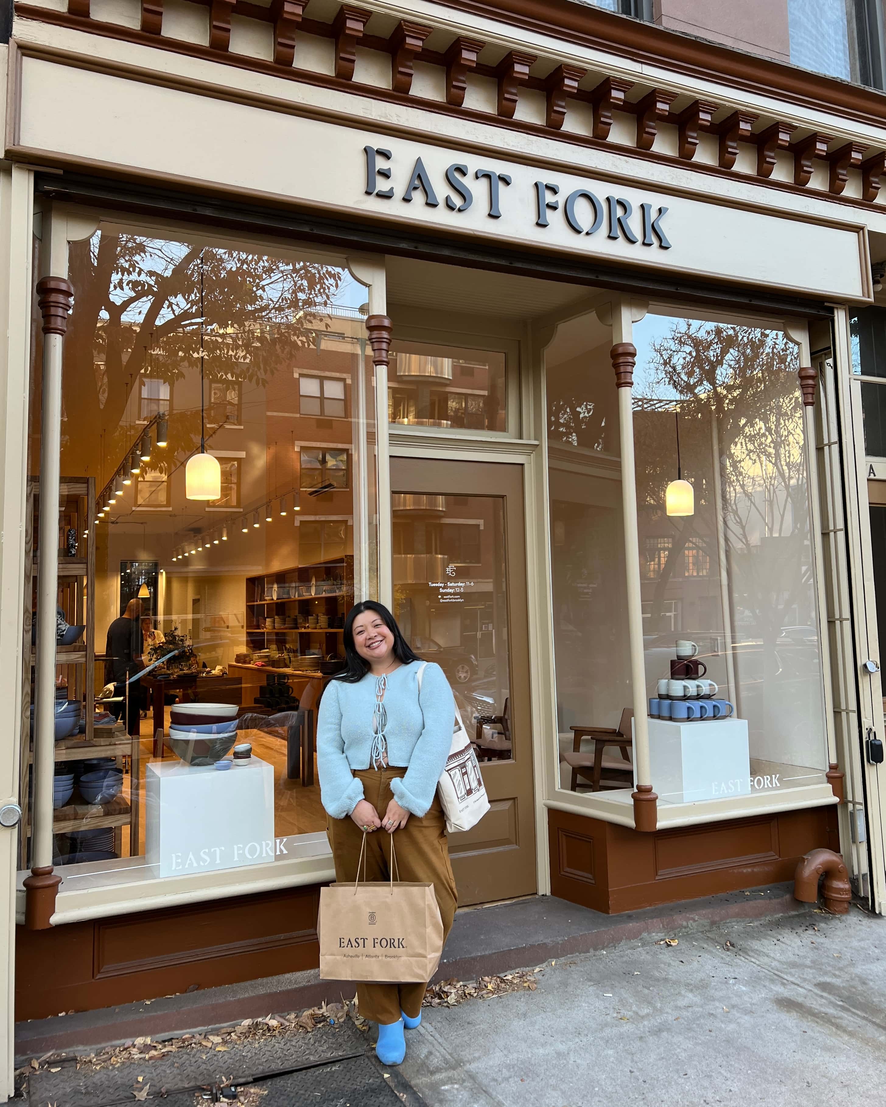Stacey standing outside the East Fork Brooklyn Store holding a shopping bag and smiling