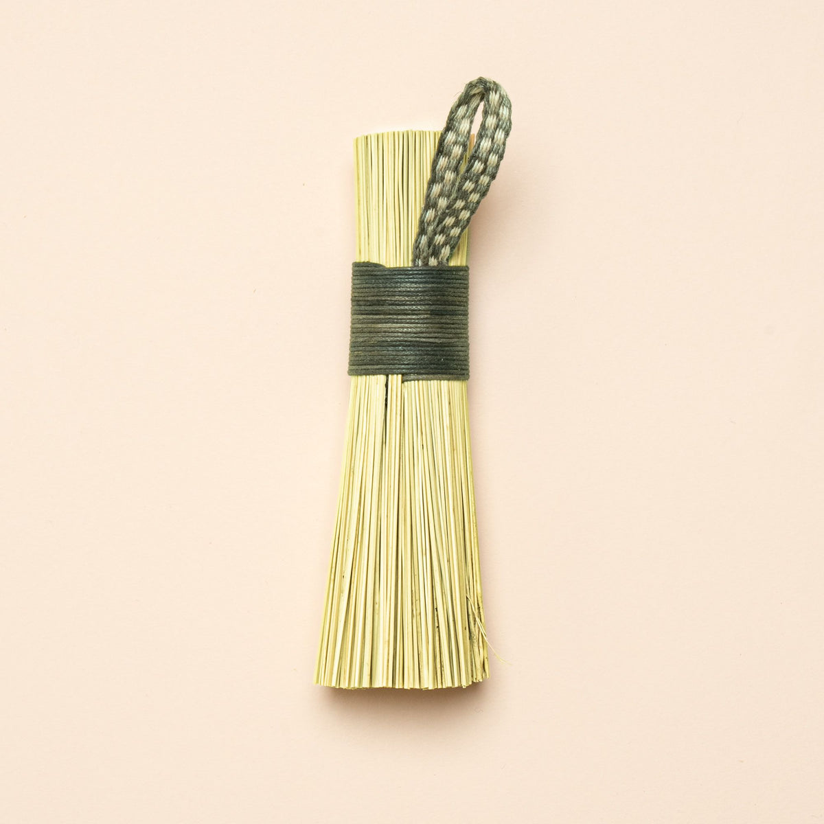 A short scrub made out of broomcorn, tied together with cotton and a loop for hanging.