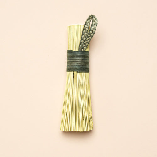 A short scrub made out of broomcorn, tied together with cotton and a loop for hanging.