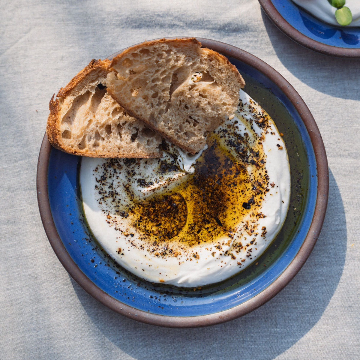 A medium sized plate in a cobalt blue color with a dip and olive oil, and 2 pieces of bread.