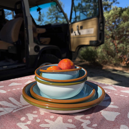 A stack of enamel plates and bowls outside on a table in front of a camper van