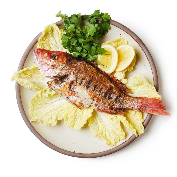 A spread of fish on a large ceramic platter in a warm, tan-toned, off-white color featuring iron speckles and an unglazed rim.