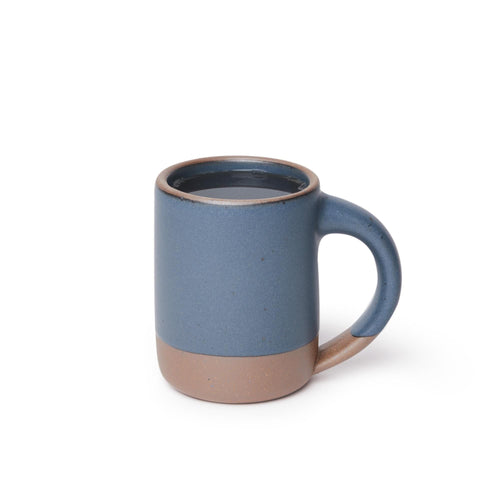 A medium sized ceramic mug filled with coffee with handle in a cool medium blue color featuring iron speckles and unglazed rim and bottom base.