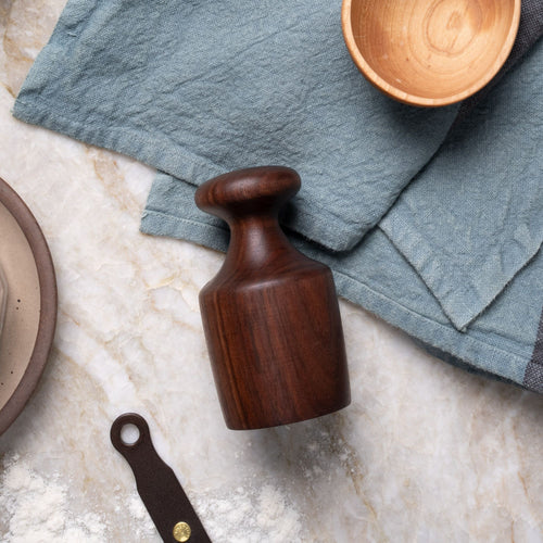 Dark wooden biscuit cutter on a marble countertop, surrounded by a blue linen cloth, small wooden bowl, and a dusting of flour.