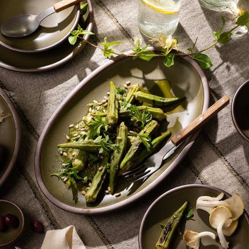 Olive-toned stoneware oval platter, styled with grilled okra and herbs on a rustic linen table.