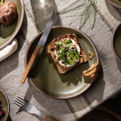 Olive-toned stoneware dinner plate, styled with artisanal toast and seasonal toppings on a rustic linen table.