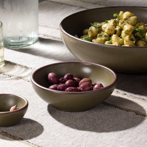 Olive-toned stoneware shallow bowl filled with olives, shown alongside coordinating tableware.