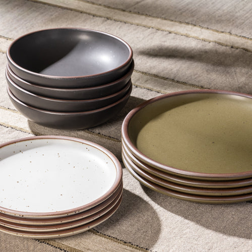 Stack of 4 dinner plates in an olive green color, 4 side plates in an off-white color, and 4 everyday bowls in a graphite black color.