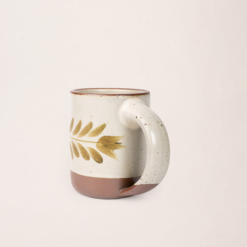 Side profile of a Warm off-white ceramic mug with a hand-painted olive green leaf motif and exposed clay base on a plain white background.