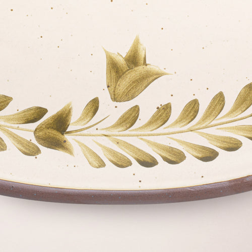 Closeup of an Oval ceramic platter with a hand-painted olive green leaf and flower border on a cream background with an exposed clay rim.