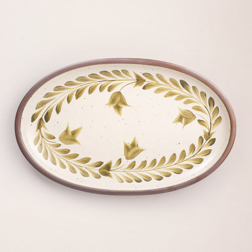 Oval ceramic platter with a hand-painted olive green leaf and flower border on a cream background with an exposed clay rim.