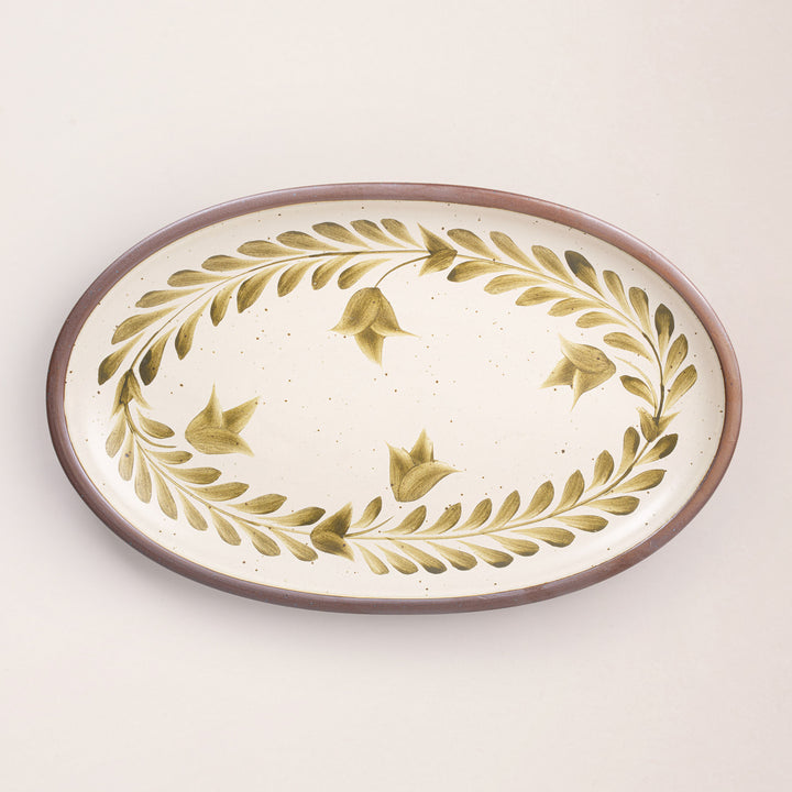Oval ceramic platter with a hand-painted olive green leaf and flower border on a cream background with an exposed clay rim.