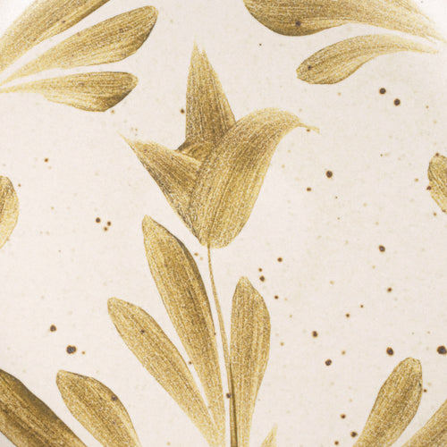 Closeup of a small round ceramic plate with a hand-painted olive green flower and leaf design on a cream background with an exposed clay rim.