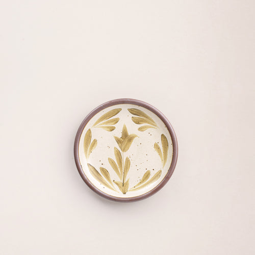 Small round ceramic plate with a hand-painted olive green flower and leaf design on a cream background with an exposed clay rim.