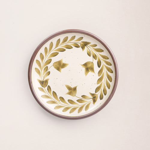 Dinner round ceramic plate with a hand-painted olive green leaf wreath and floral design on a cream background with an exposed clay rim.