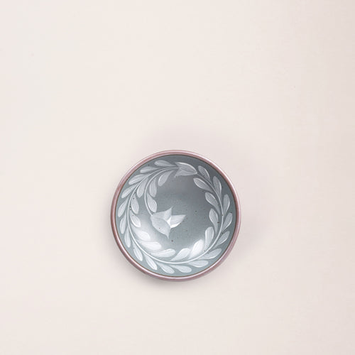 Overhead of a Small ceramic shallow bowl with a hand-painted white leaf border on a blue-grey interior and exterior with an exposed clay rim.