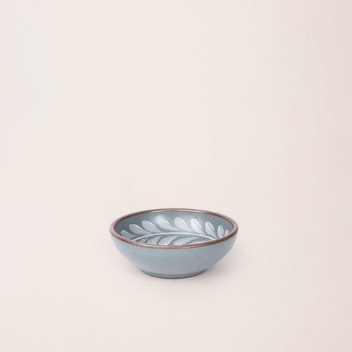 Small ceramic shallow bowl with a hand-painted white leaf border on a blue-grey interior and exterior with an exposed clay rim.